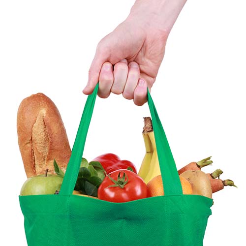 Hand holding a reusable shopping bag filled with fruits and vegetables